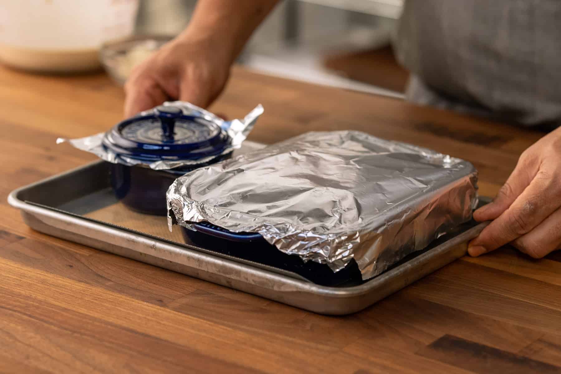 baking dishes covered with aluminum foil and on a baking sheet.