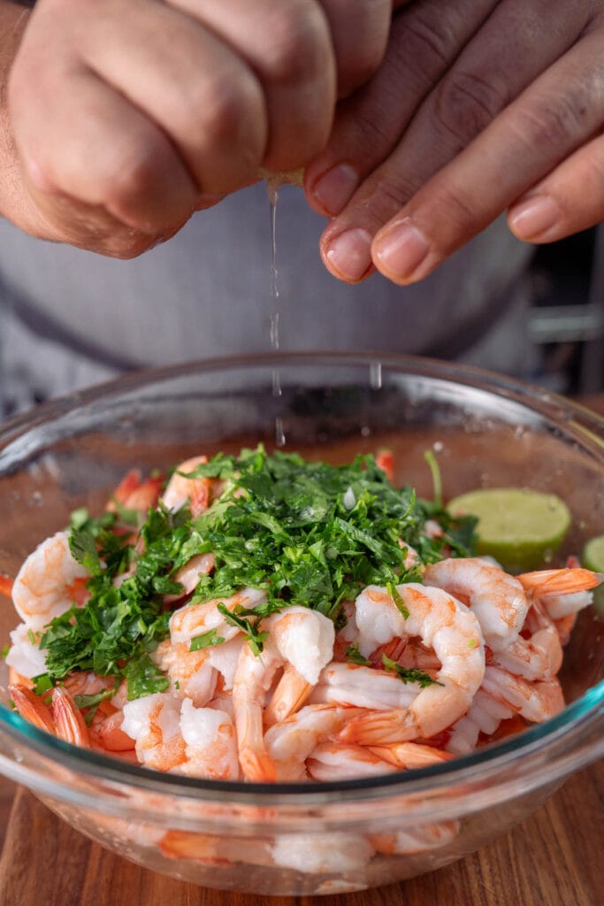 lime being squeezed over a bowl filled with cooked shrimp and chopped cilantro.